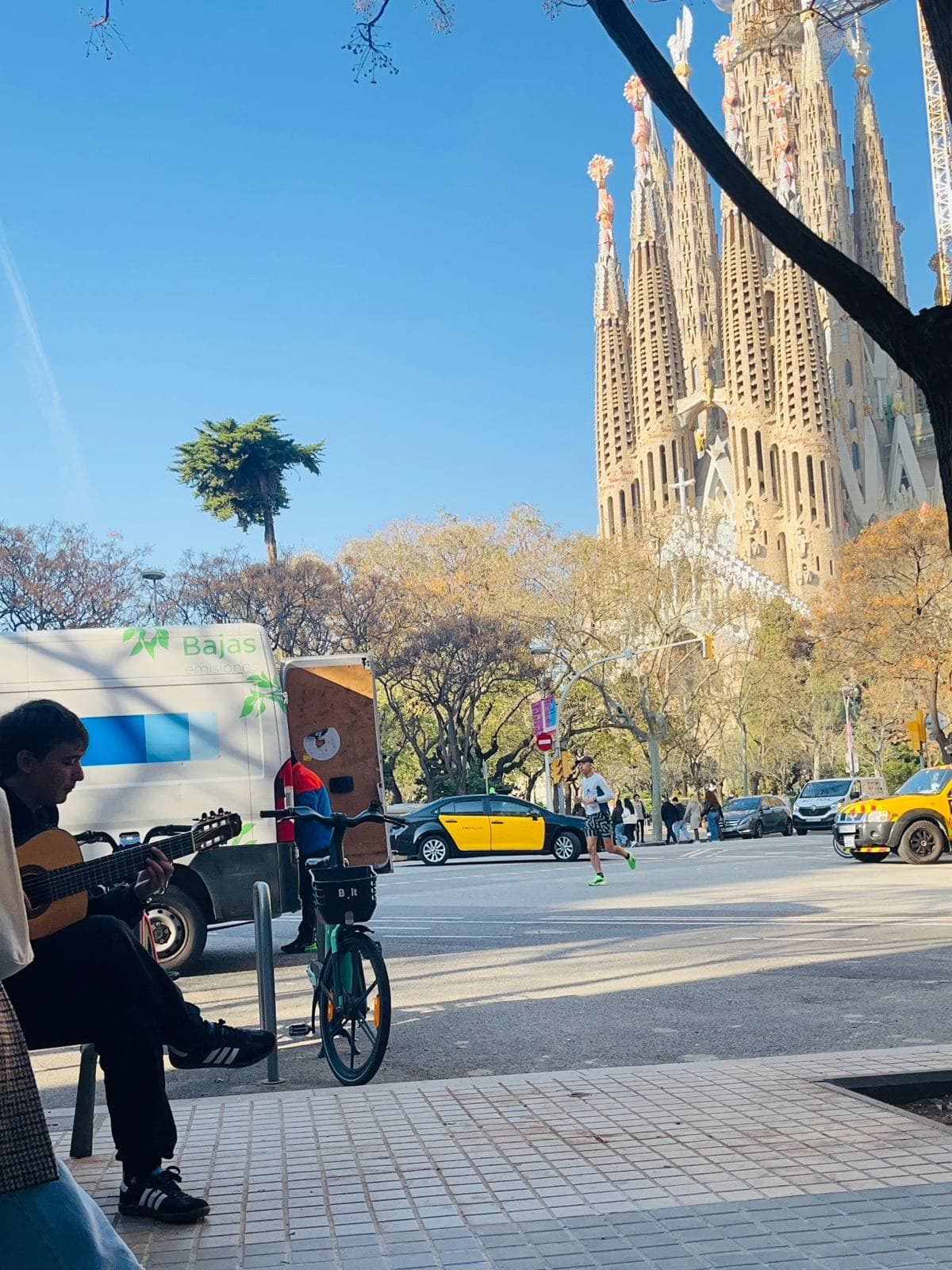 Lisandro sentado en un banco tocando la guitarra, con la Sagrada Família de fondo.