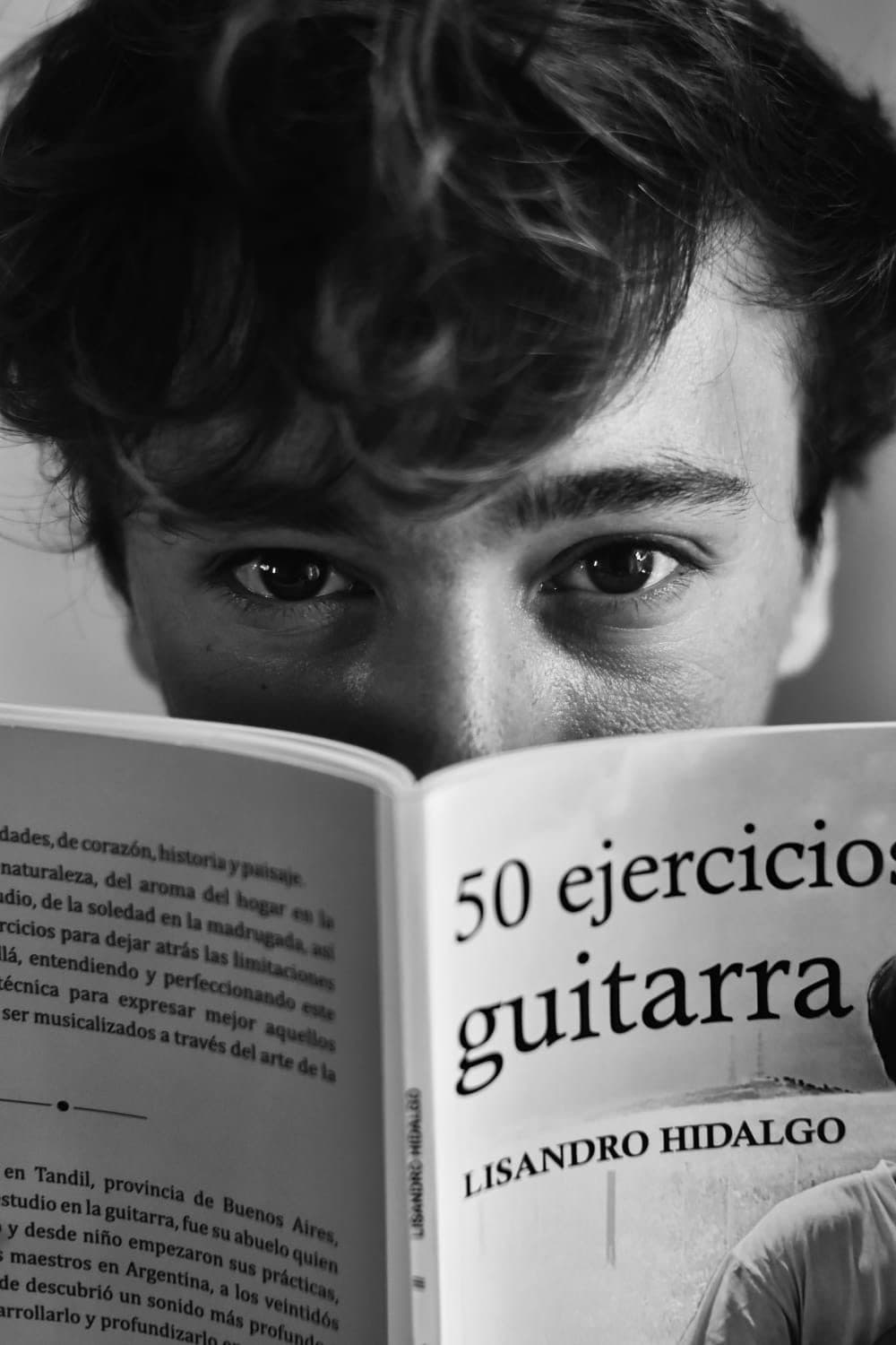 Lisandro con el libro abierto tapándole media cara, mirando a la cámara.