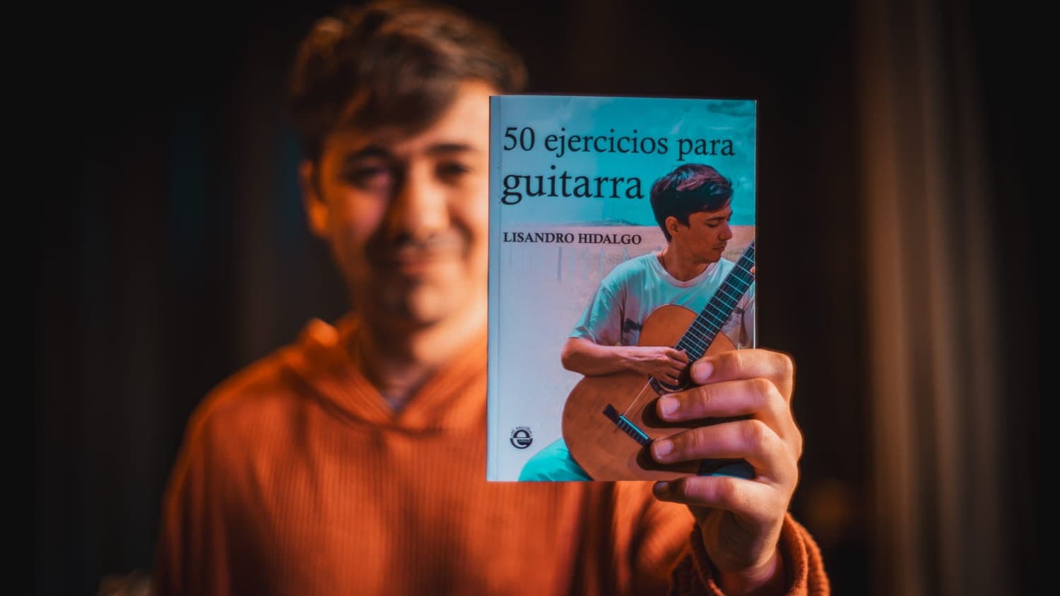 Lisandro sosteniendo su libro «50 ejercicios para guitarra» frente a la cámara.